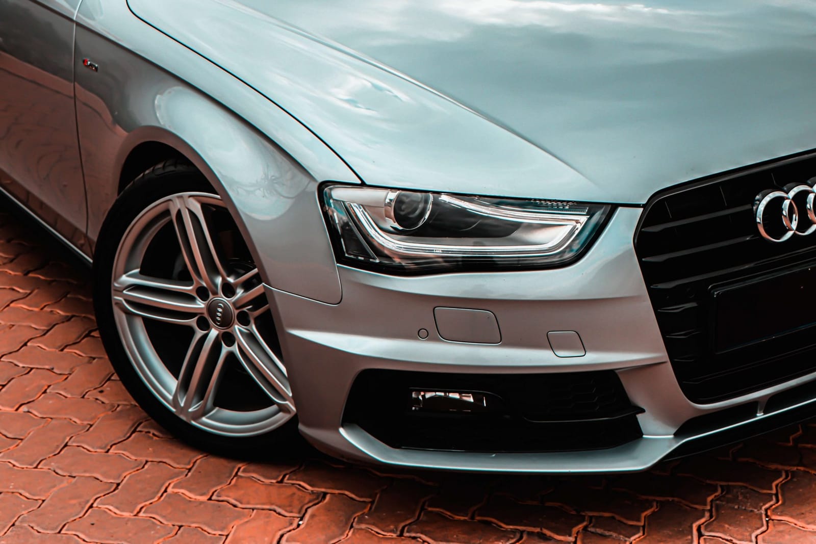 Front corner of a silver Audi A4 showing the headlight and alloy wheel