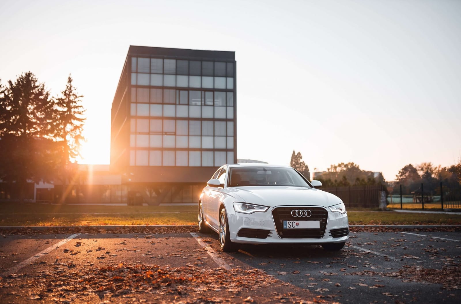 White Audi A6 sedan parked in front of an office building at sunset