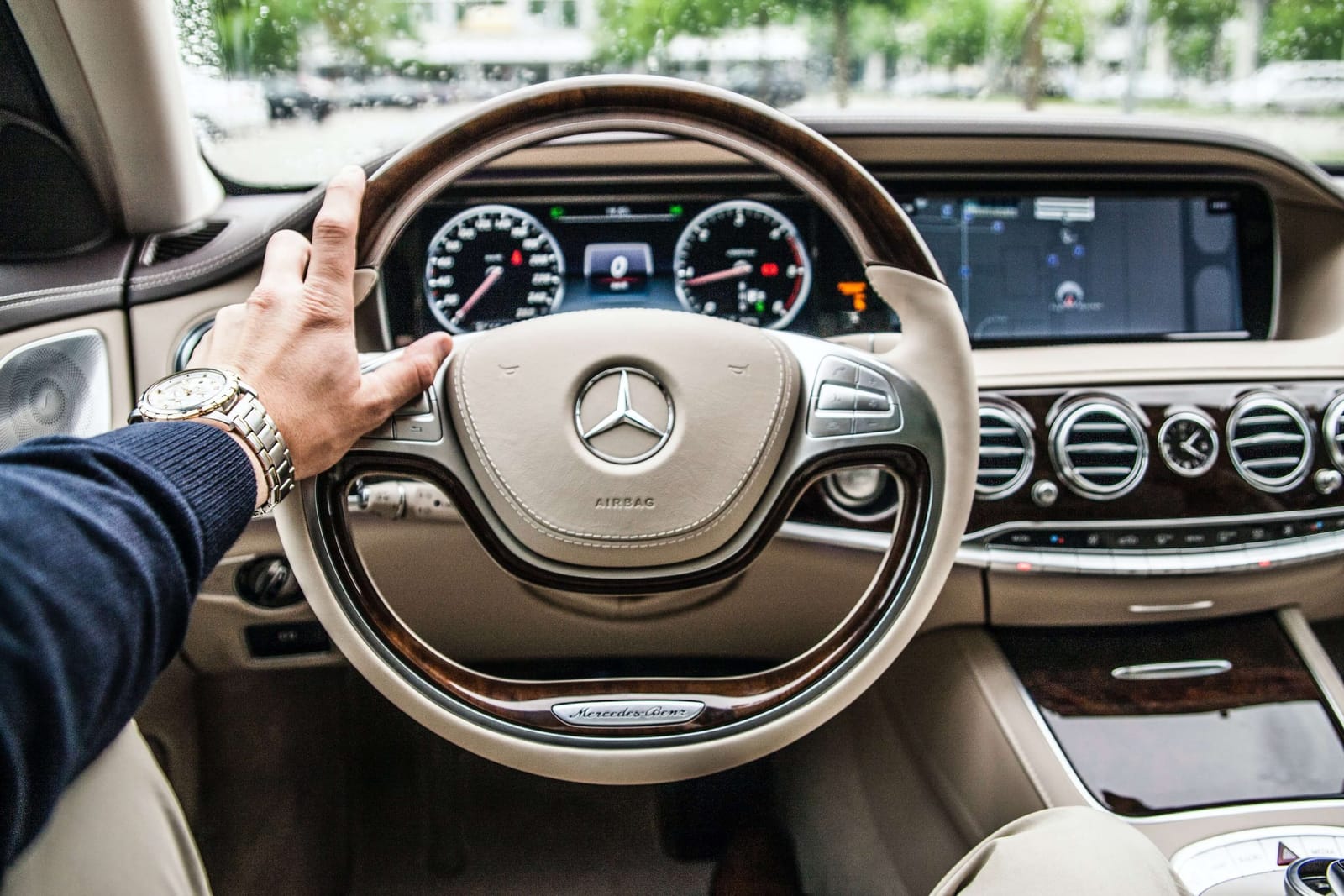 Driver's hand on the wood and cream leather steering wheel of a Mercedes-Benz